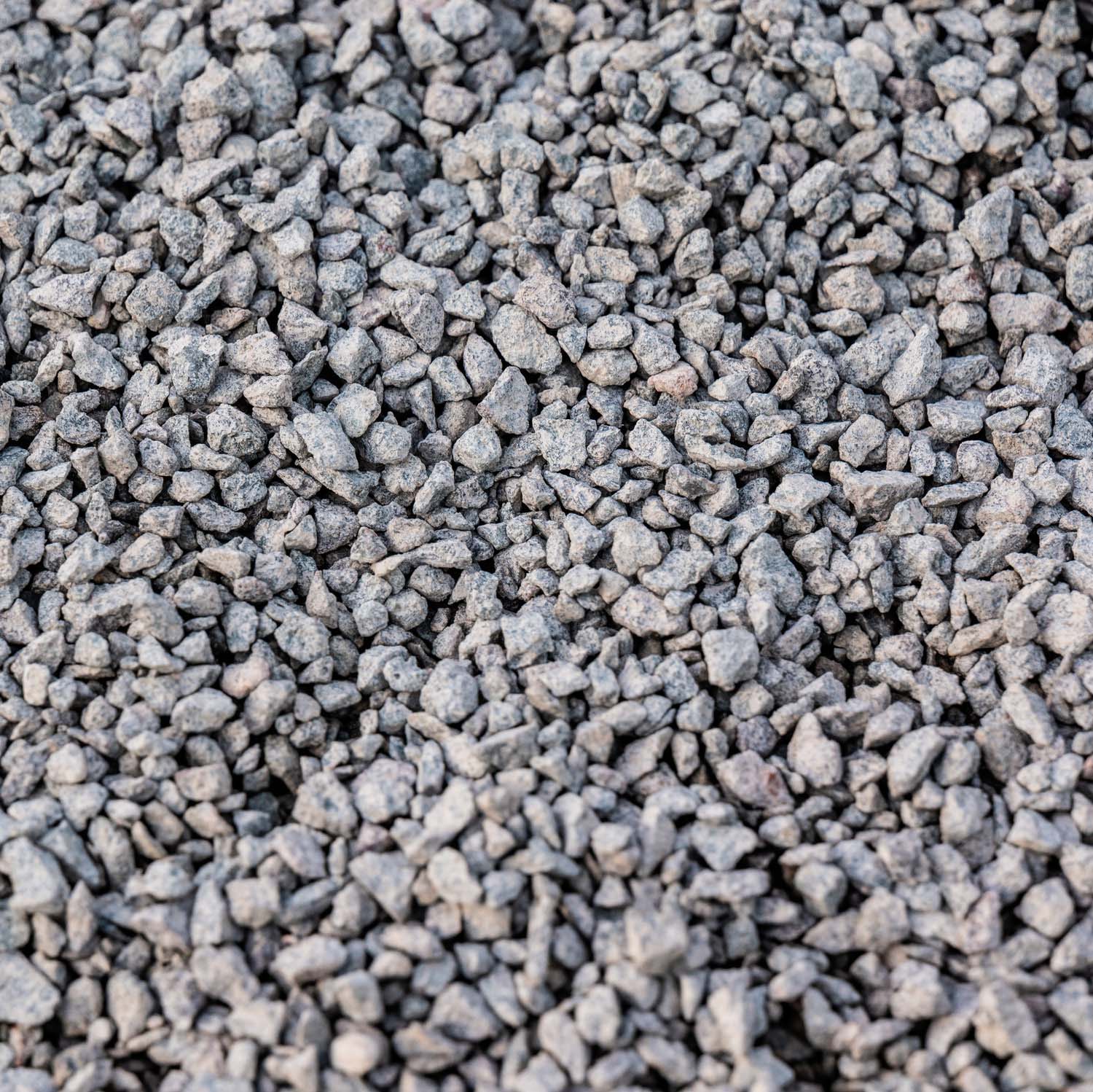 Nahaufnahme von grauem Splitt mit unregelmäßigen, kantigen Partikeln. Die Steine sind in verschiedenen Grautönen gehalten und haben eine raue, körnige Textur. Der Splitt besteht aus gebrochenem Gestein und zeigt eine gleichmäßige Verteilung der Körner.